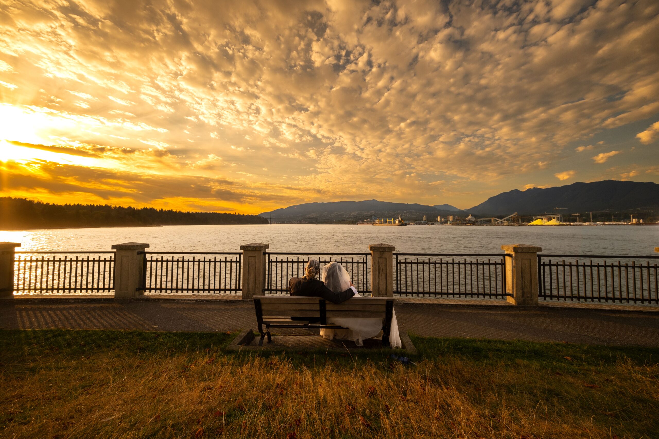 Couple sitting by the Vancouver waterfront at sunset with mountains across the harbour